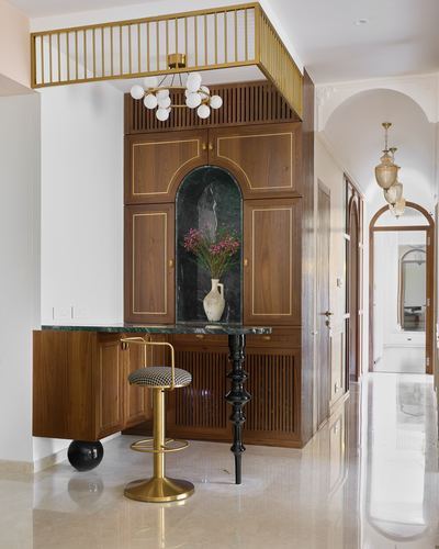 Wooden foyer cabinet with arched marble niche, brass railing above, and houndstooth bar stool