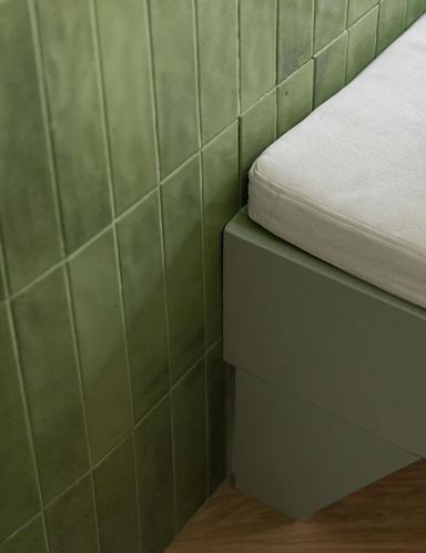 Close-up corner of green textured tile wall meeting a green bench with cream cushion