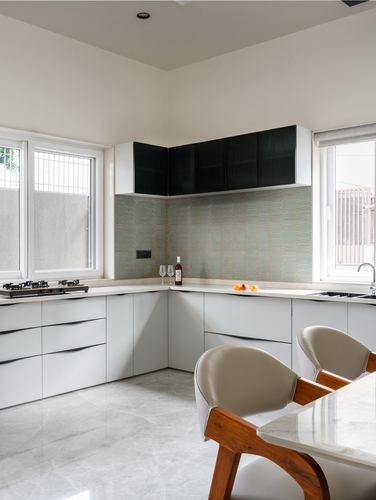 White L-shaped kitchen with black upper cabinets, patterned backsplash, and marble-look floor