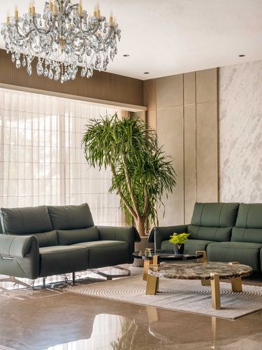 Living room with green leather sofas, marble coffee tables, crystal chandelier, and tall plant by window