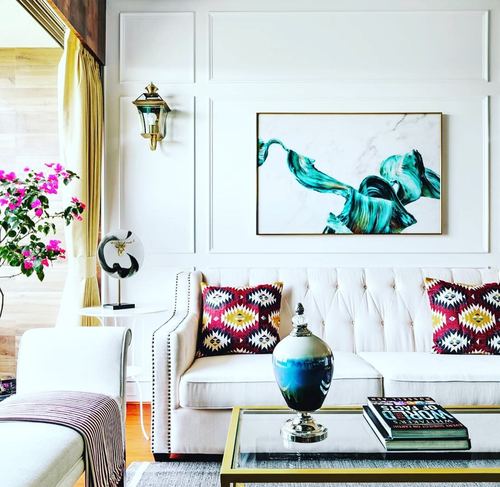 White tufted sofa with kilim cushions beneath a teal abstract painting on paneled wall