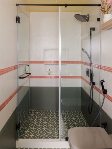 Glass-enclosed shower with green patterned floor tile and terracotta striped wall border