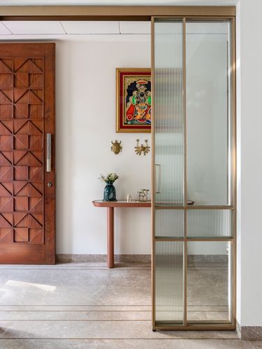 Foyer with carved wooden door, fluted glass partition, and tanjore painting above a terracotta console table