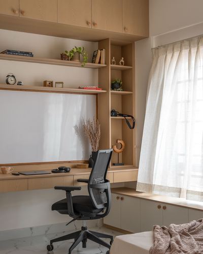 Wooden study nook with open shelves, built-in desk, mesh office chair, and sheer curtained window.