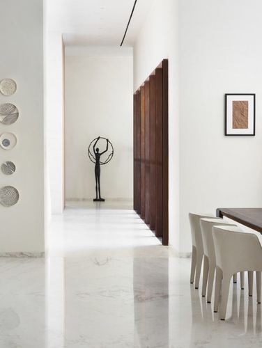 Minimalist corridor with polished stone floor, sculpture, fluted wood wall, and dining area beyond