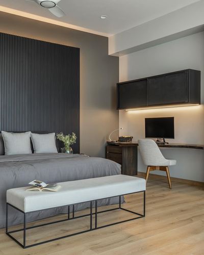 Minimalist bedroom with fluted charcoal headboard wall, grey bedding, bench, and built-in study desk with dark cabinet.