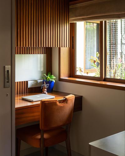 Wooden study nook with fluted paneling, desk, orange chair, and window
