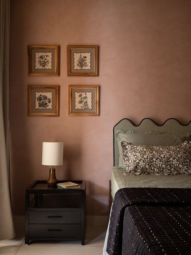 Bedroom with pink textured wall, framed botanical prints, and scalloped green headboard