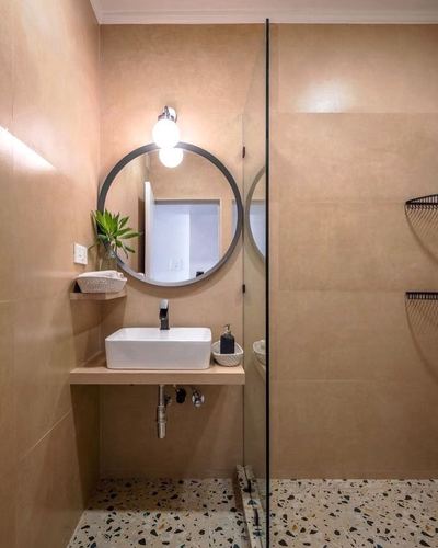 Beige-tiled bathroom with round black-framed mirror, vessel sink, and terrazzo floor