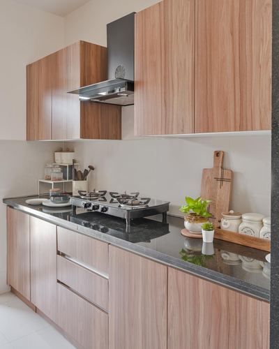 L-shaped modern kitchen with wood cabinetry, black countertop, gas stove and chimney hood