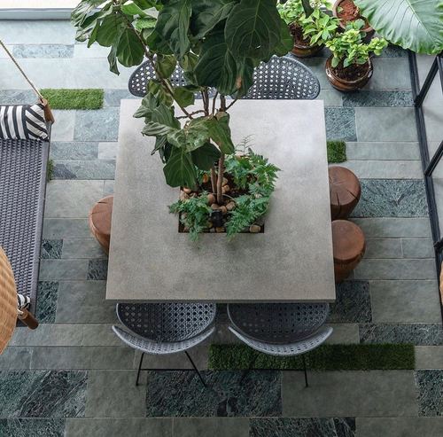 Overhead view of courtyard table with central planter tree, cane chairs, stone flooring with grass inlays