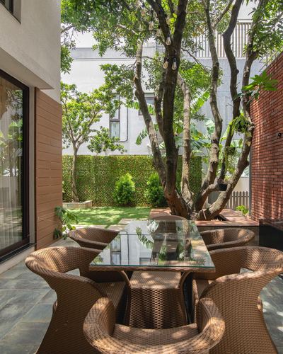 Outdoor patio with glass-top wicker dining set beneath a large tree, brick wall alongside