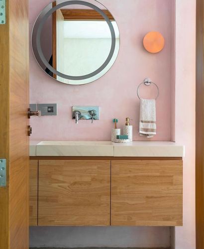 Pink plaster bathroom with round mirror, wood vanity, and orange wall sconce