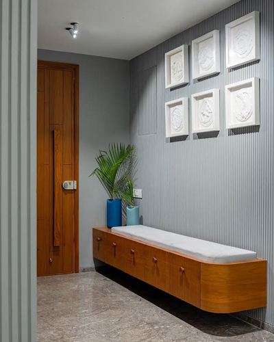 Grey fluted-panel foyer wall with white art pieces above a floating wooden bench and teal vases