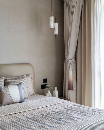 Beige bedroom corner with curved headboard, alabaster pendant lights, and tasseled curtain
