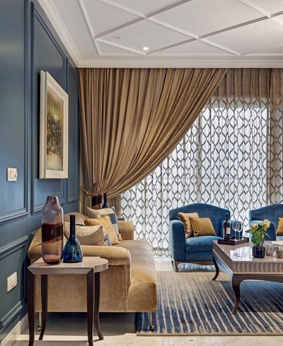 Living room with blue paneled walls, gold curtains, velvet armchairs and a marble coffee table