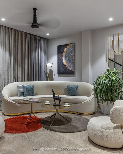Curved cream sofa with layered rugs and gold-trimmed coffee tables in a neutral living room