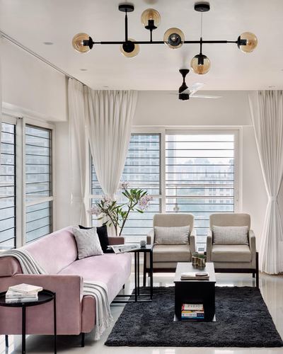 Living room with pink velvet sofa, cream armchairs, black coffee table on dark rug, sheer curtains and glass chandelier