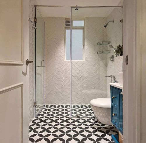 White herringbone-tiled bathroom with glass shower, black-and-white floor, blue vanity