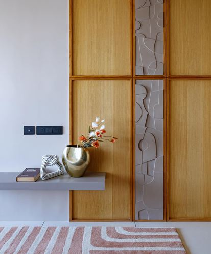 Wood-panelled foyer wall with floating console holding brass vase and flowers, striped pink rug below