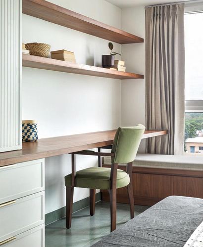 Study nook with floating wood shelves, olive chair at desk, and window seat beside curtained window