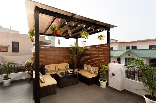 Rooftop pergola lounge with rattan sofas, wooden slat wall, and hanging plants in Gurugram home