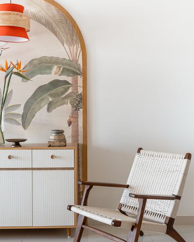 Foyer with arched tropical wallpaper, wooden sideboard, and cane-woven lounge chair