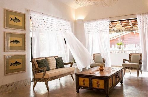 Sunlit living room in Goa home with distressed wooden sofa, trunk coffee table and framed fish prints