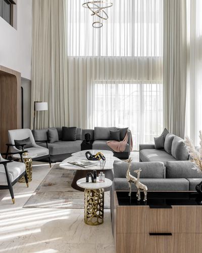 Double-height living room with grey sectional sofas, marble tables, and floor-to-ceiling sheer curtains