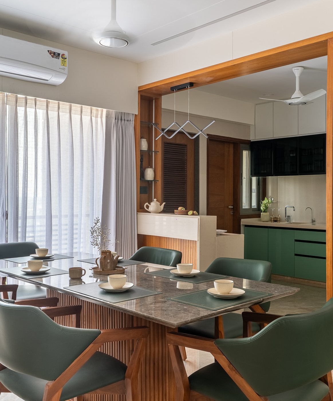 Dining room with marble-look table, green leather chairs, and view into green kitchen beyond