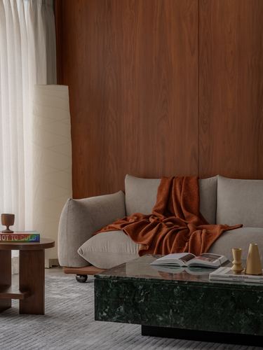 Beige sofa with rust throw against walnut-panelled wall, green stone coffee table in front