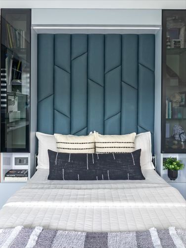 Bed with teal geometric upholstered headboard flanked by glass cabinets, patterned pillows