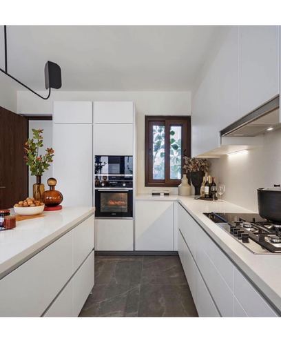 All-white galley kitchen with island counter, built-in oven, and dark stone floor