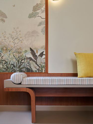 Wooden bench with striped cushion beneath a framed botanical mural in a foyer