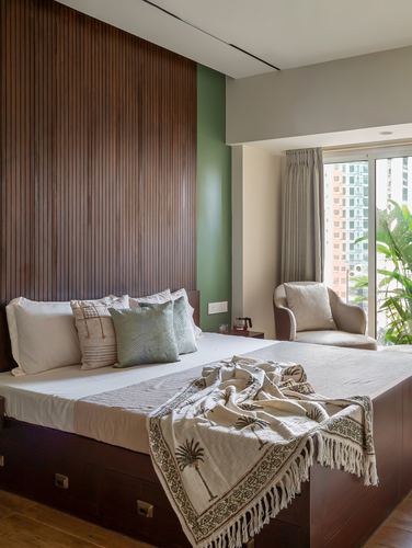 Bedroom with fluted wood paneled headboard wall, platform bed, and armchair by window overlooking city