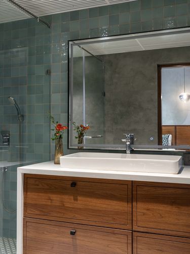 Bathroom vanity with wood drawers, white vessel sink, teal tile wall and backlit mirror