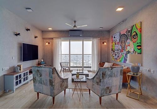 Living room with grey walls, wooden floor, patterned armchairs, and colorful pop-art canvas facing balcony view