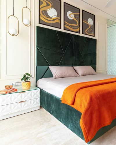 Bedroom with green faceted velvet headboard, orange throw, and abstract triptych above bed