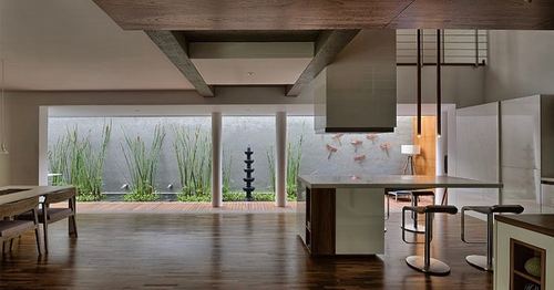 Open-plan kitchen with wood floor, island, and glazed wall overlooking a landscaped water feature.