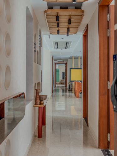 Long polished corridor with circular wall niches, wooden ceiling panel, and glimpse into a living space beyond