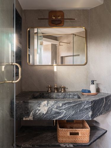 Bathroom with dark veined stone vanity, brass mirror, and woven basket below