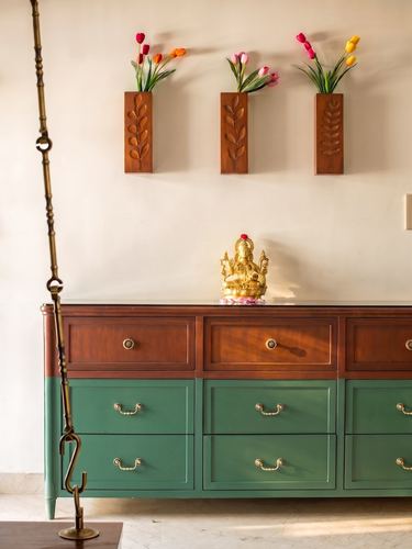 Wooden and green sideboard below three carved vases with tulips and a brass Ganesha idol