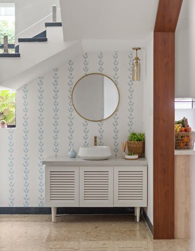Powder room vanity under a staircase with floral wallpaper and round brass mirror
