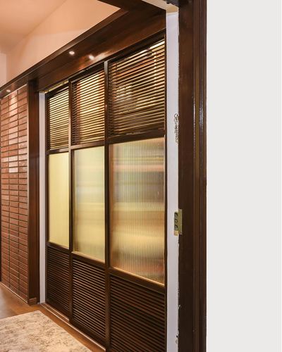 Wooden sliding door with louvered and fluted glass panels beside a brick wall