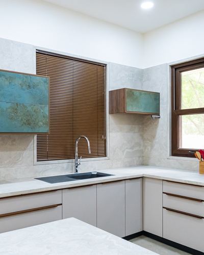 L-shaped kitchen with marble-look walls, wooden blinds, teal-fronted cabinets, and stone countertops