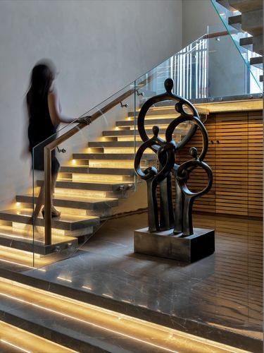 Woman ascends glowing cantilevered stone staircase beside bronze sculpture and wooden slat wall