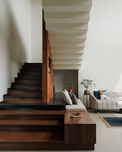 Wooden cantilevered staircase with dark stone risers beside a beige sofa nook in a minimal home.