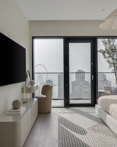 Neutral-toned bedroom with black-framed windows overlooking a city skyline and a tufted bed