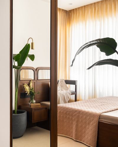 Mirror reflecting wood-panelled bedside nook beside sunlit bedroom with sheer curtains and pink bedspread