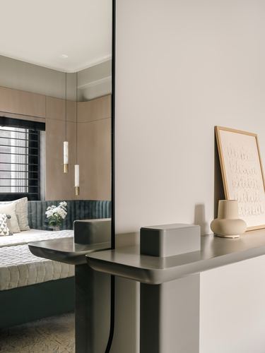 Foyer console beside mirror reflecting a tufted bench and bedroom beyond